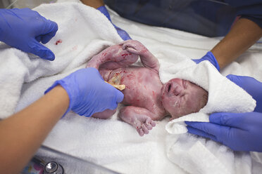 Abgeschnittene Hände von Ärzten, die einen neugeborenen Jungen in einer Krippe im Krankenhaus halten - CAVF56304