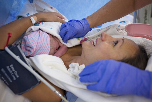 Abgeschnittene Hände des Arztes von der Mutter, die ihr Neugeborenes stillt, während sie auf dem Bett im Krankenhaus liegt - CAVF56305