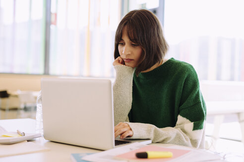 Frau, die einen Laptop benutzt, während sie am Tisch in einer Bibliothek sitzt - CAVF56310