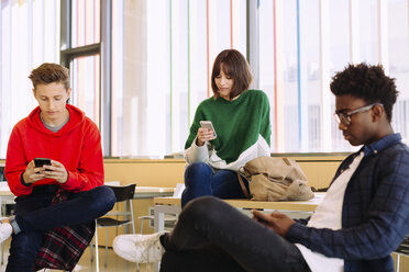 Studenten, die in der Bibliothek sitzen und Mobiltelefone benutzen - CAVF56313