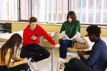 Studenten, die in der Bibliothek sitzen und Smartphones benutzen - CAVF56317