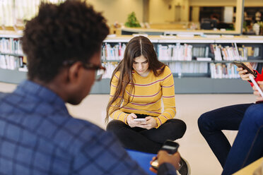 Freunde benutzen Smartphones, während sie in der Bibliothek sitzen - CAVF56318