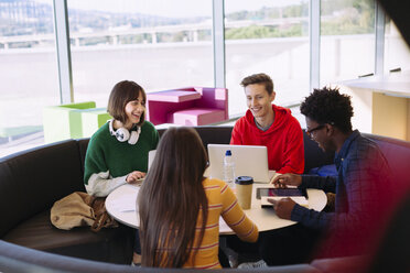 Lächelnde Freunde, die in einer Bibliothek am Fenster sitzen und diskutieren - CAVF56339