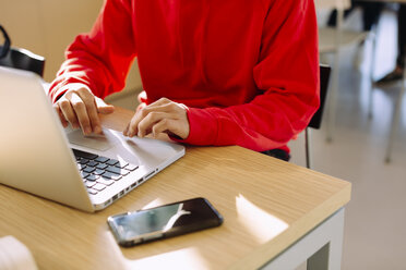 Midsection of man using laptop computer while sitting at table in library - CAVF56349