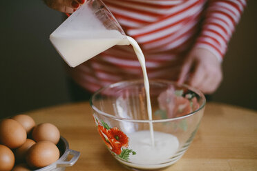 Mittelteil einer Frau, die Milch in eine Schüssel auf einem Holztisch zu Hause gießt - CAVF56384