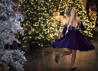 Rear view of happy girl dancing by illuminated Christmas trees at night - CAVF56391