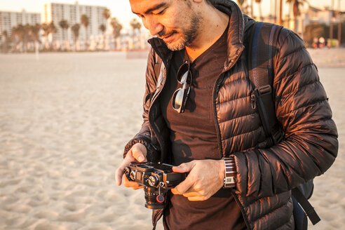 Mann trägt Jacke und hält Kamera am Strand - CAVF56394