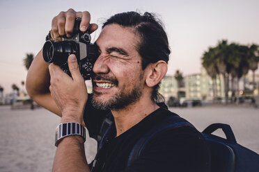 Nahaufnahme eines Rucksacktouristen, der am Strand mit seiner Kamera fotografiert - CAVF56397