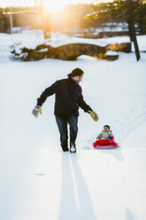 Vater zieht Schlitten mit Tochter auf verschneitem Feld im Park - CAVF56416