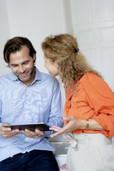 Glückliches Paar, das von zu Hause aus arbeitet und über ein digitales Tablet diskutiert - HHLMF00558
