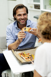 Happy couple sitting in the garden, eating pizza, drinking wine - HHLMF00605