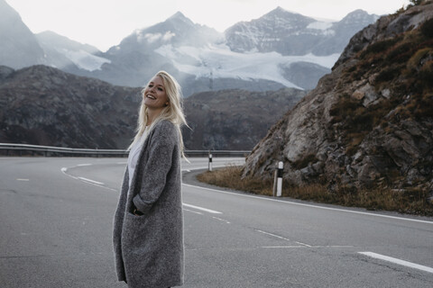 Schweiz, Engadin, glückliche junge Frau am Strassenrand in Berglandschaft stehend, lizenzfreies Stockfoto