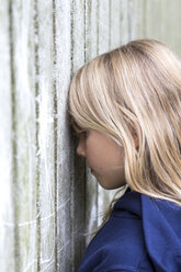 Profil eines traurigen blonden Mädchens, das an einer Holzwand lehnt - JFEF00929
