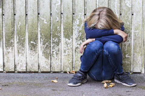 Sad girl crouching in front of wooden wall hiding her face stock photo