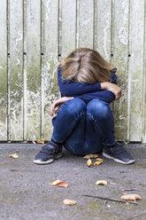 Trauriges Mädchen hockt vor einer Holzwand und versteckt ihr Gesicht - JFEF00937