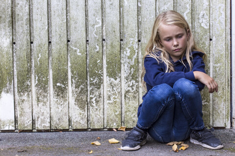 Porträt eines traurigen Mädchens, das vor einer Holzwand sitzt, lizenzfreies Stockfoto