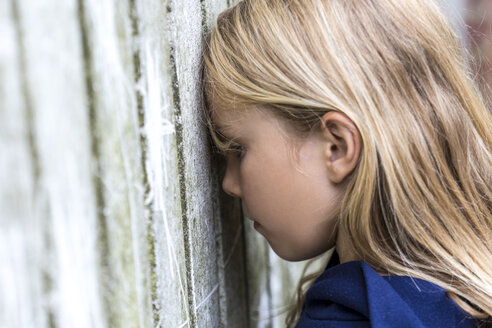 Profile of sad blond girl leaning against wooden wall - JFEF00943