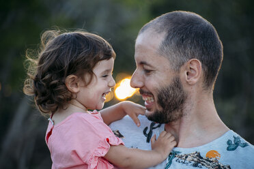 Glücklicher Vater hält seine Tochter bei Sonnenuntergang im Freien - GEMF02573