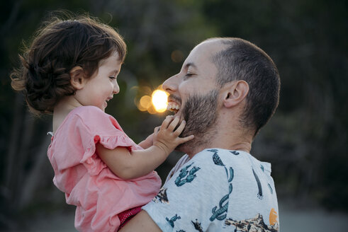 Glücklicher Vater hält seine Tochter bei Sonnenuntergang im Freien - GEMF02575