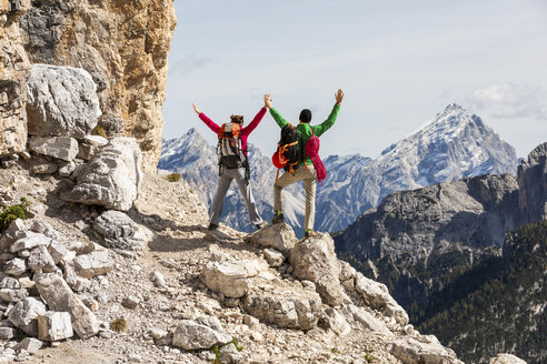 Italy, Cortina d'Ampezzo, couple with rope and climbing equipment looking at view with raised arms - WPEF01134