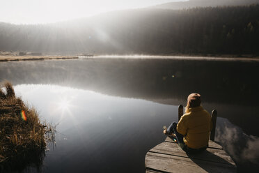 Switzerland, Engadine, Lake Staz, woman sitting on a jetty at lakeside in morning sun - LHPF00143