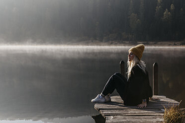 Switzerland, Engadine, Lake Staz, woman sitting on a jetty at lakeside in morning sun - LHPF00144