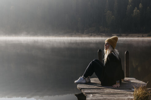 Schweiz, Engadin, Stazersee, Frau sitzt auf einem Steg am Seeufer in der Morgensonne - LHPF00144