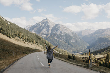 Switzerland, Engadin, rear view of happy woman with raised arms on mountain road - LHPF00149