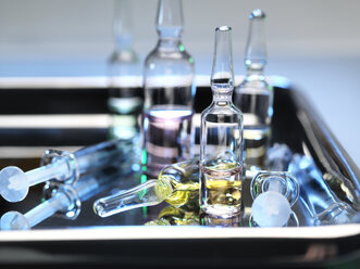 Ampules and phials containing a drug dose next to syringes on a surgical tray - ABRF00243