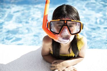 Portrait of little girl wearing snorkel and oversized diving goggles leaning on poolside - ERRF00162