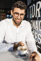 Porträt eines lachenden jungen Geschäftsmannes, der in einem Straßencafé Kaffee trinkt - TCF05970