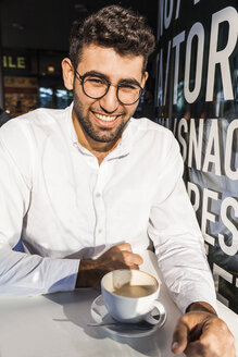 Portrait of laughing young businessman drinking coffee at sidewalk cafe - TCF05970