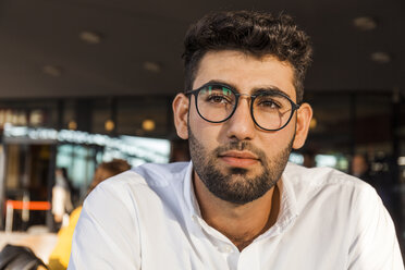 Portrait of pensive young businessman with beard and glasses at sidewalk cafe - TCF05973