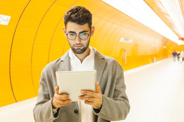 Deutschland, München, Porträt eines jungen Geschäftsmannes, der in einer U-Bahn-Station ein digitales Tablet benutzt - TCF05997