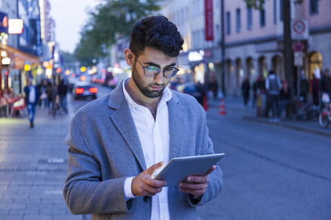 Germany, Munich, young businessman using digital tablet in the city at dusk stock photo