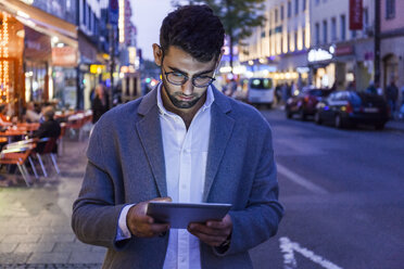 Germany, Munich, young businessman using digital tablet in the city at dusk - TCF05999