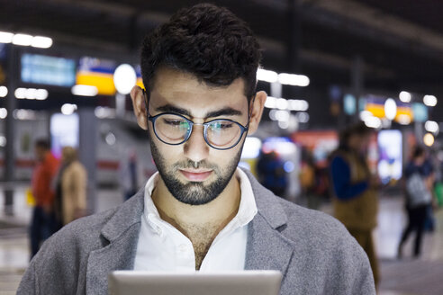 Germany, Munich, portrait of young businessman using digital tablet at central station - TCF06003