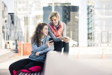 Freundinnen, die nach dem Training eine Pause machen und ihr Smartphone benutzen - MOEF01673