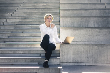 Junge Geschäftsfrau sitzt auf einer Treppe und benutzt einen Laptop - MOEF01683