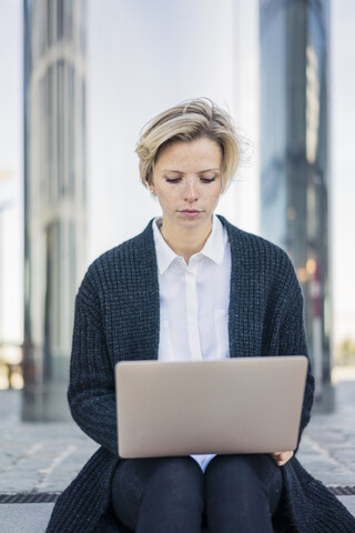 Junge Geschäftsfrau sitzt auf einer Treppe und benutzt einen Laptop, lizenzfreies Stockfoto