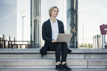Junge Geschäftsfrau sitzt auf einer Treppe und benutzt einen Laptop - MOEF01691