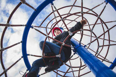 Low angle portrait of boy climbing merry-go-round against cloudy sky - CAVF56468