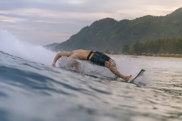 Mann ohne Hemd surft auf dem Meer gegen den bewölkten Himmel bei Sonnenuntergang - CAVF56522