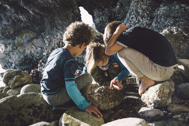 Freunde spielen mit Steinen, während sie sich am Strand zusammenkauern - CAVF56526