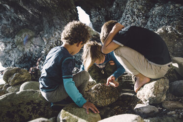 Friends playing with rocks while crouching at beach - CAVF56526