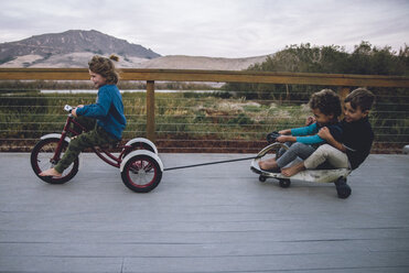 Junge zieht Spielzeugauto mit Freunden und fährt Dreirad auf dem Boden - CAVF56527