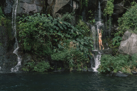 Frau im Bikini genießt Wasserfall im Wald, lizenzfreies Stockfoto