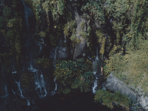 Mittlere Entfernung einer Frau im Bikini, die einen Wasserfall im Wald genießt, lizenzfreies Stockfoto