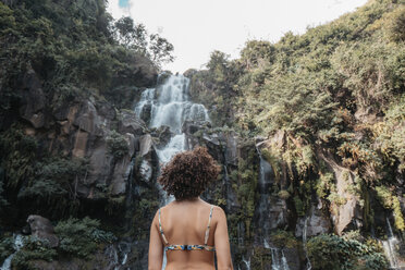 Rückansicht einer Frau im Bikini, die vor einem Wasserfall im Wald steht - CAVF56536