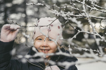 Porträt eines niedlichen, fröhlichen Mädchens, gesehen durch schneebedeckte, getrocknete Pflanzen - CAVF56542